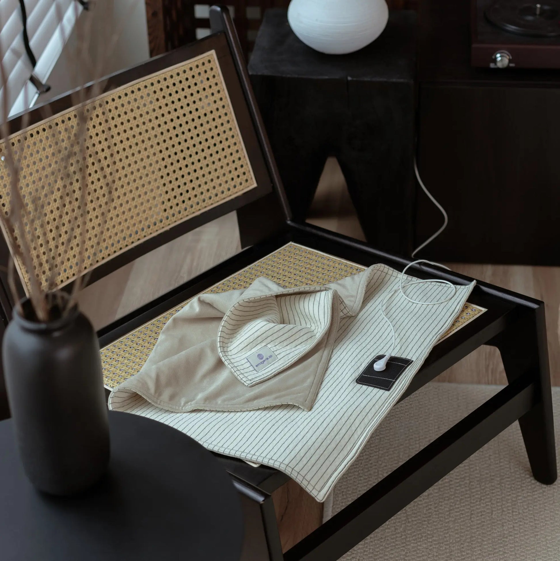 Modern rattan chair with a beige heating pad and remote, Emagene Life wellness product