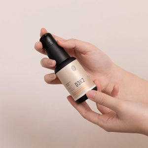 Hand holding Emagene Life D3K2 supplement bottle, minimalist beige background
