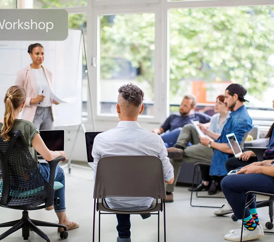 Group workshop in modern office, presenter at whiteboard, participants with laptops and tablets