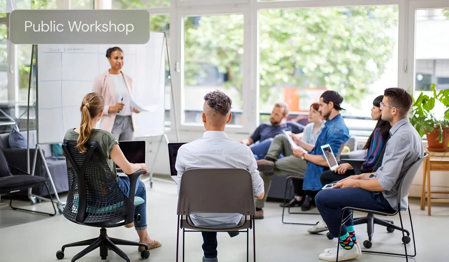 Group workshop in modern office, presenter at whiteboard, participants with laptops and tablets